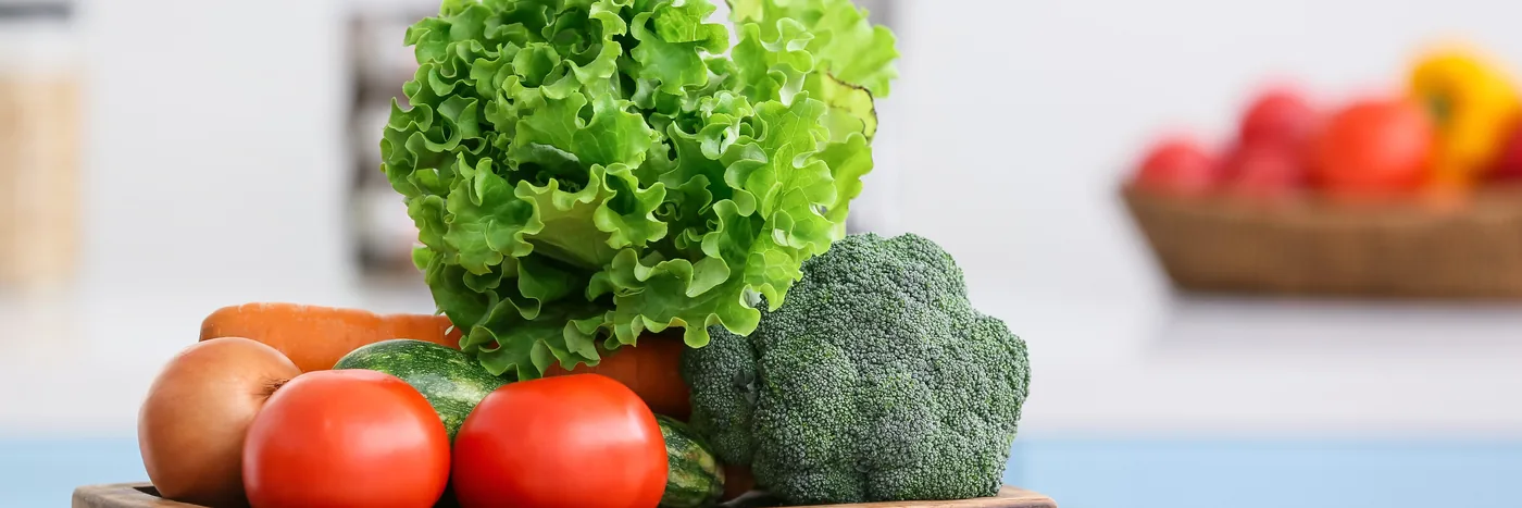 A wooden board of fresh vegetables -- lettuce, broccoli, tomatoes and peppers -- on a bright kitchen counter.