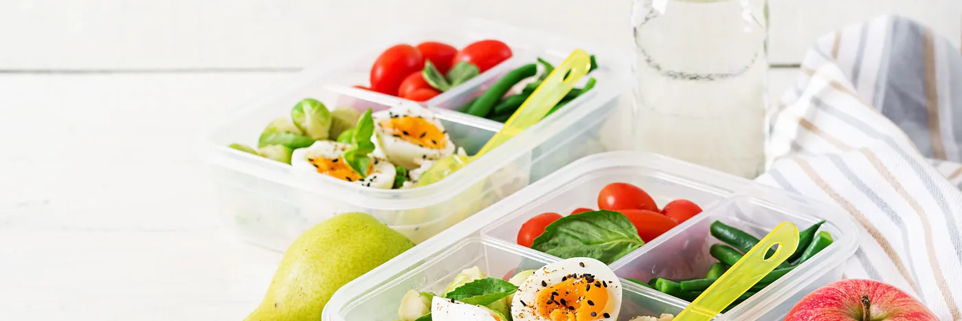 Prepared meal containers filled with vegetables, greens and tomatoes, ready for the week.
