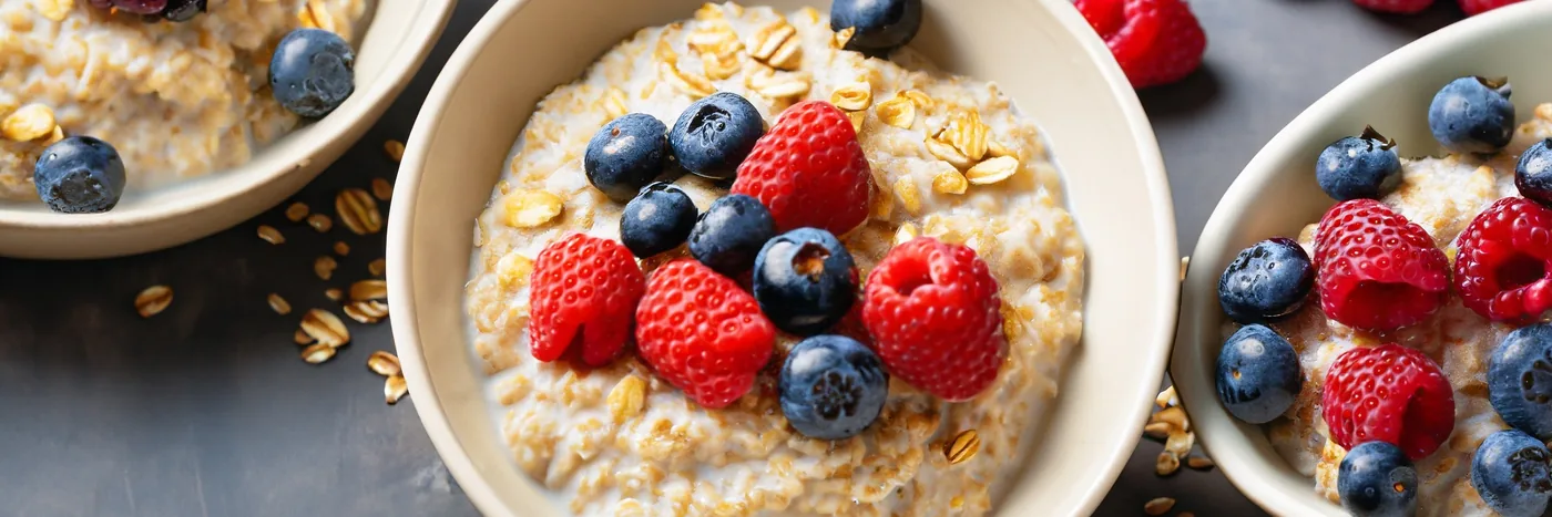 A bowl of oatmeal topped with raspberries and blueberries beside a second bowl of oats.