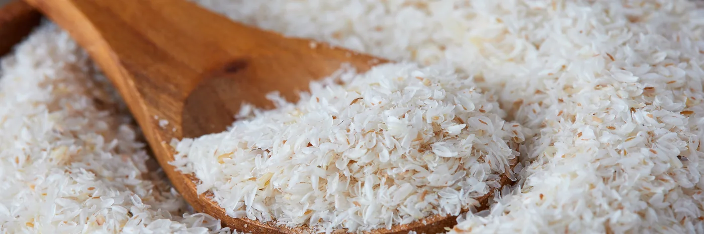 Loose psyllium husk heaped on a wooden spoon, spilling onto a pale surface.