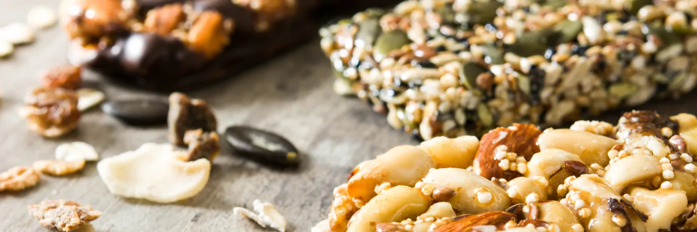 Homemade seed and nut bars on a wooden table with loose walnuts, cashews and pumpkin seeds.